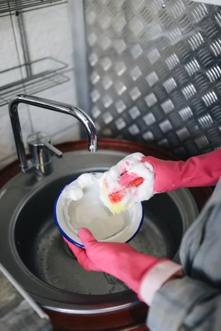A woman in a red uniform cleans indoors with a blue bucket, ensuring a spotless environment.